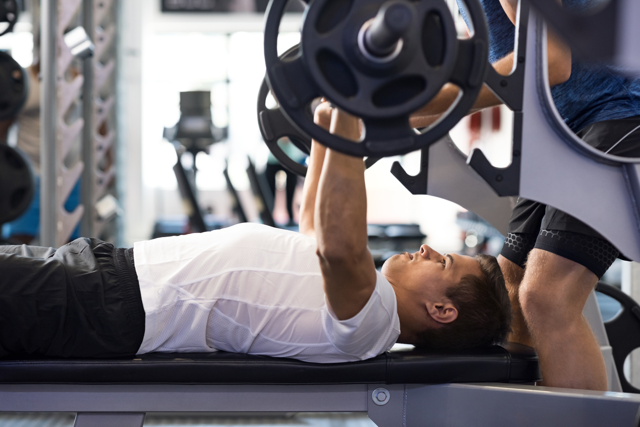 Man doing bench press A male athlete undergoing APRE training with a personal trainer.