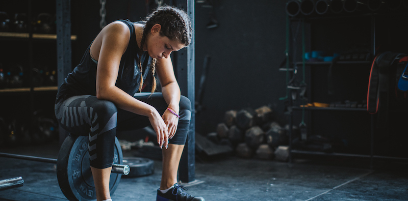 Tired female athlete sitting on a barbell at the gym 